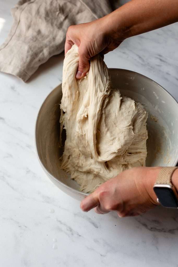 Person repeating the stretch and fold technique on sourdough bagel dough.