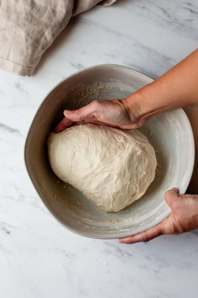 Person forming sourdough bagel dough into a smooth ball after stretching and folding.