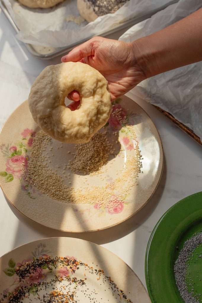 Dipping unbaked sourdough bagel in a plate of sesame seeds.