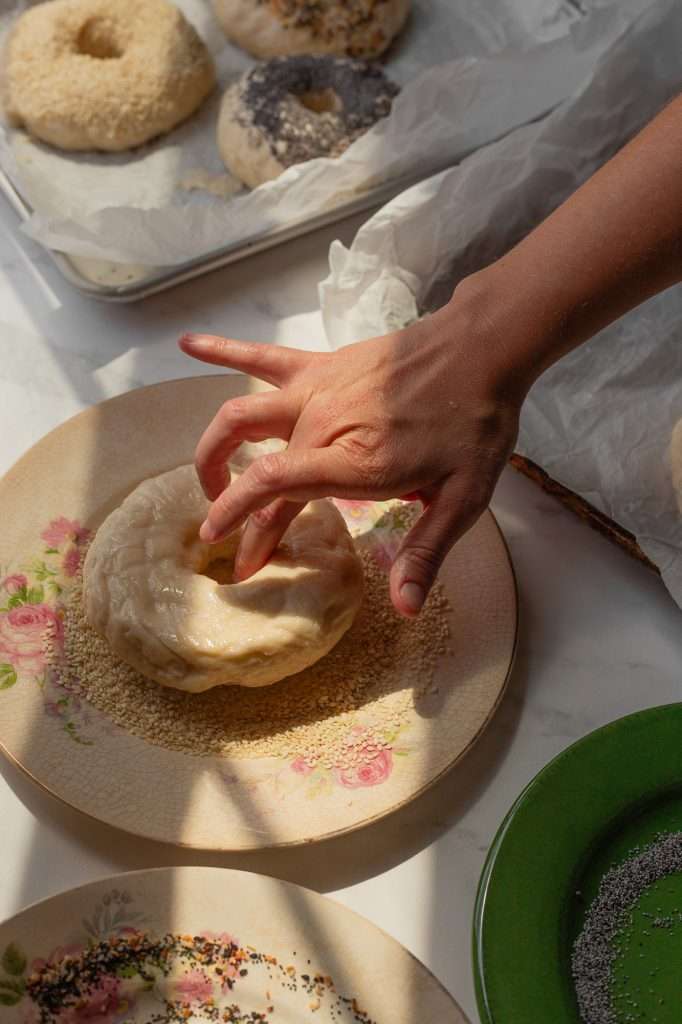 Pressing unbaked sourdough bagel into a plate of sesame seeds.