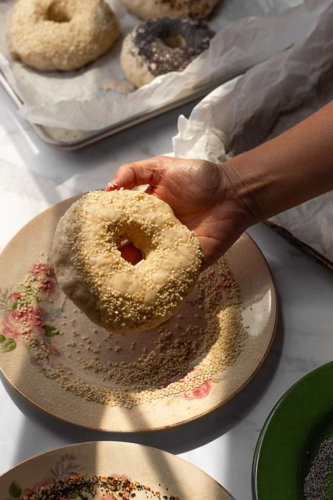 Hand holding a sourdough bagel coated with sesame seeds before baking.