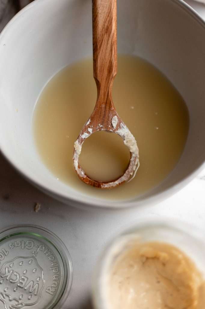 Wooden spoon resting in a bowl of sourdough starter mixture.