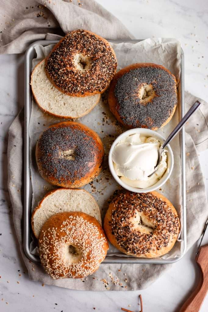 Tray of homemade sourdough discard bagels topped with poppy seeds, sesame seeds, and everything seasoning, with cream cheese on the side.