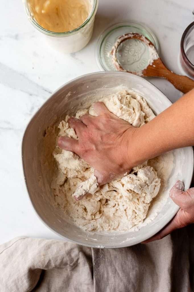 Person mixing sourdough bagel dough by hand in a bowl.