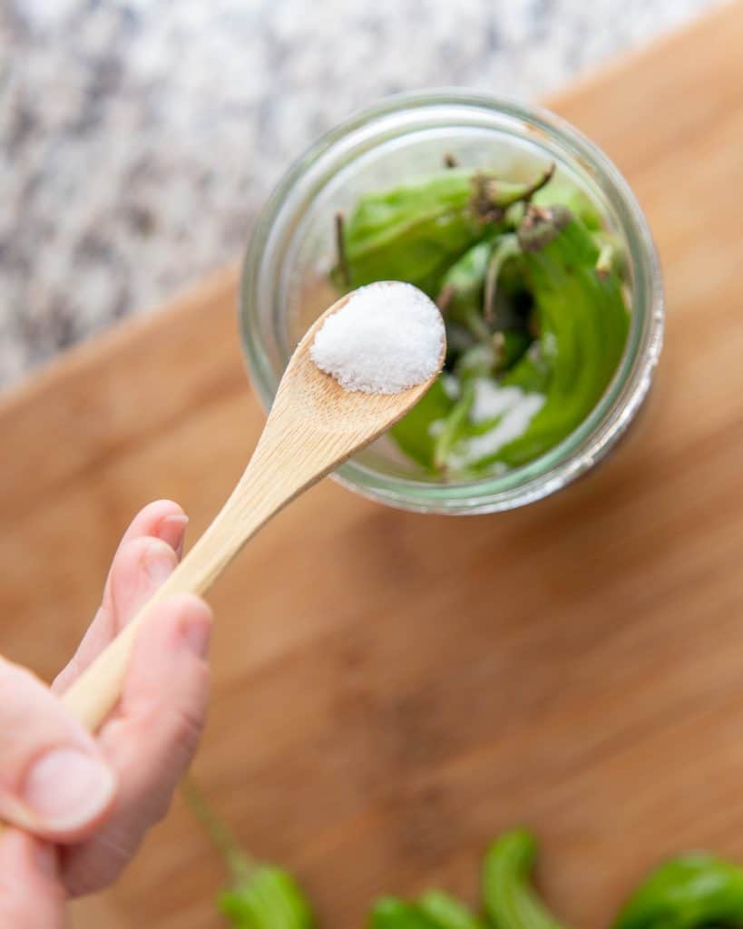 wooden spoon full of salt over a mason jar of green jalapeño peppers