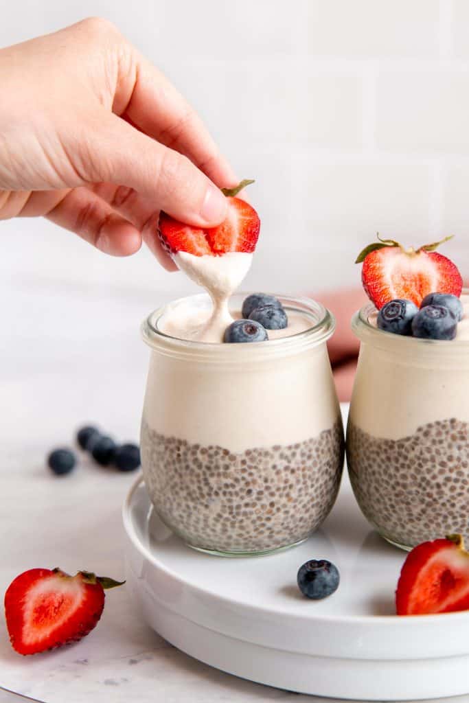 a strawberry slice being dipped into a container of chia pudding.