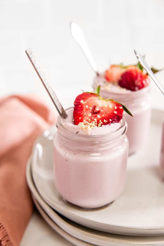 Pink Strawberry yogurt in a small glass jar, with a sliced strawberry on top