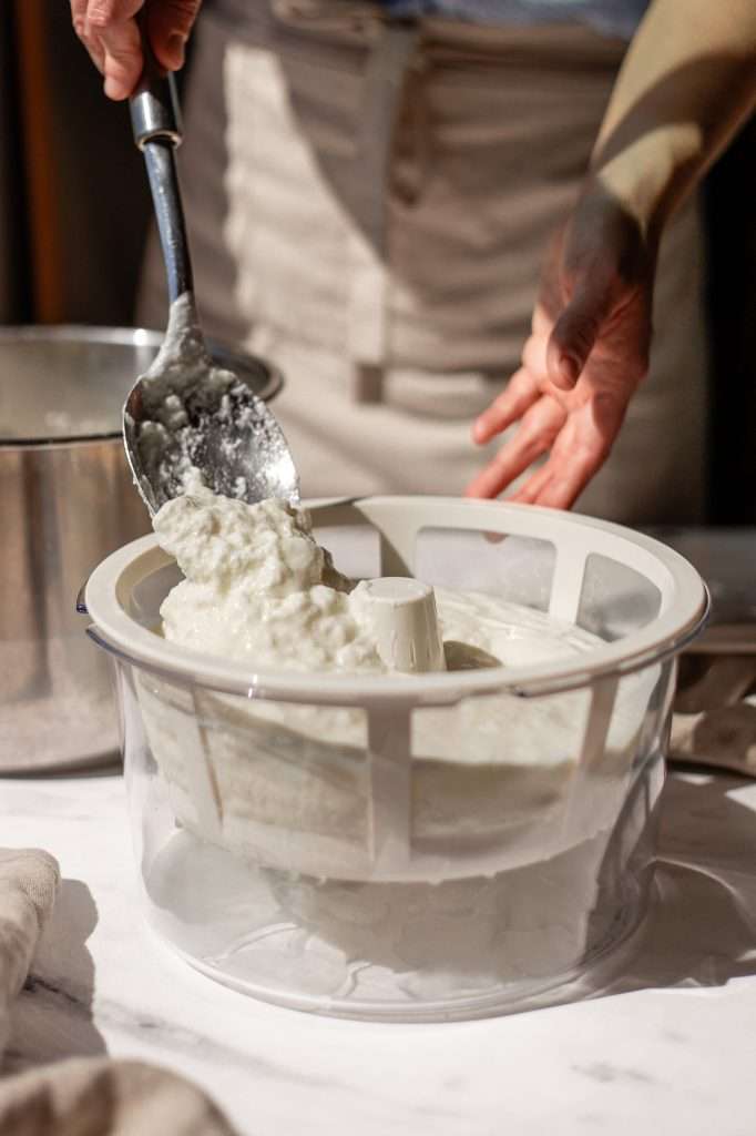 someone spooning instant pot yogurt into a greek yogurt strainer to make the yogurt thicker and smoother. 