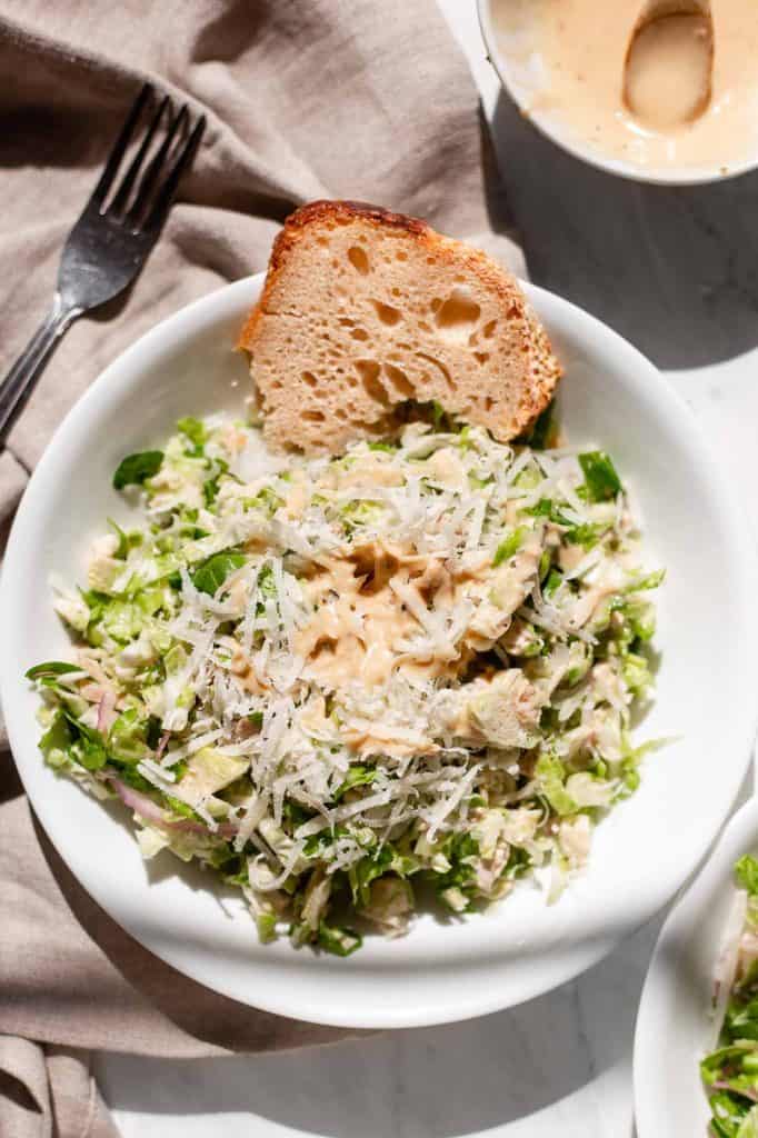 Brussel Sprout Caesar Salad topped with freshly shaved Parmesan and served with a side of crusty sourdough bread. 