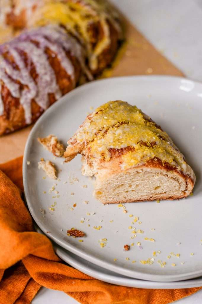 a piece of sourdough cinnamon roll king cake on a white plate with a bit taken out of it. 