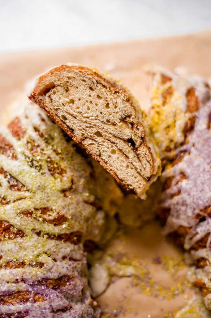 A slice of sourdough king cake is lifted, revealing its soft, airy crumb with delicate cinnamon swirls. 