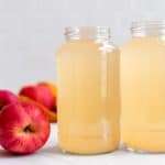 Two jars of homemade fermented fruit vinegar with fresh apples in the background.