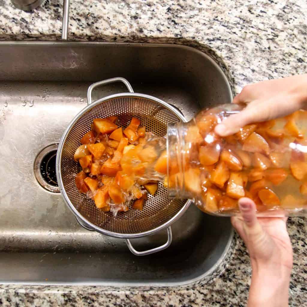 Pouring fermented fruit mixture through a strainer into a sink.