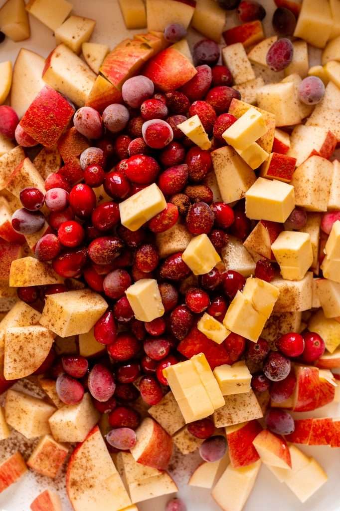 pumpkin cobbler recipe fist step, combining apples, cranberries, butter and cinnamon in a white baking dish as the base of apple pumpkin cobbler.