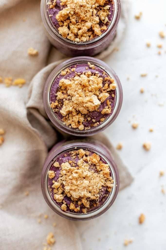 the tops of three jars of purple blackberry cobbler chia pudding, topped with gluten free granola crumbles. 