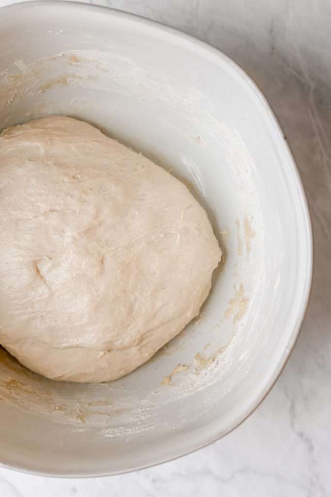 a rough dough ball in a white bowl made with this sourdough naan bread recipe. 