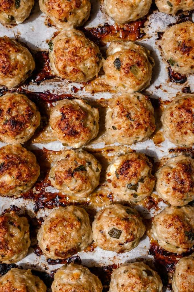 just cooked chicken zucchini meatballs on a parchment paper lined baking pan. the meatballs are lined up in rows and cooked until lightly browned. 