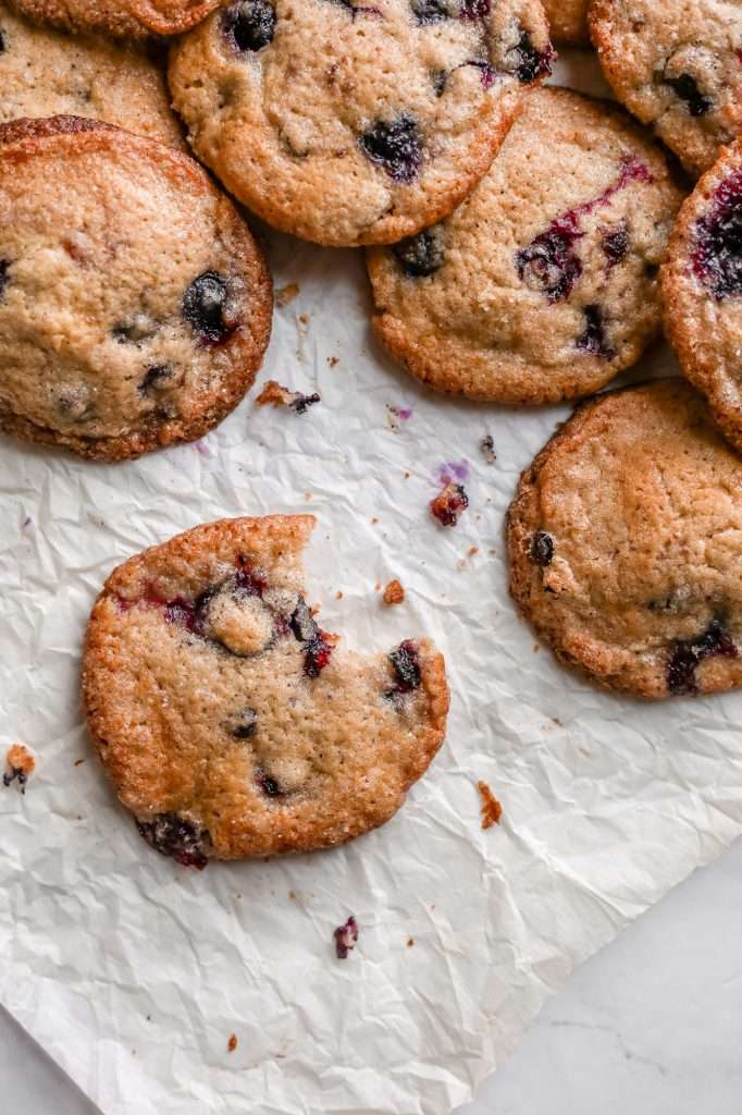 lemon blueberry cookies on a piece of crinkly white parchment paper. one cookie has a bite taken out of it. 