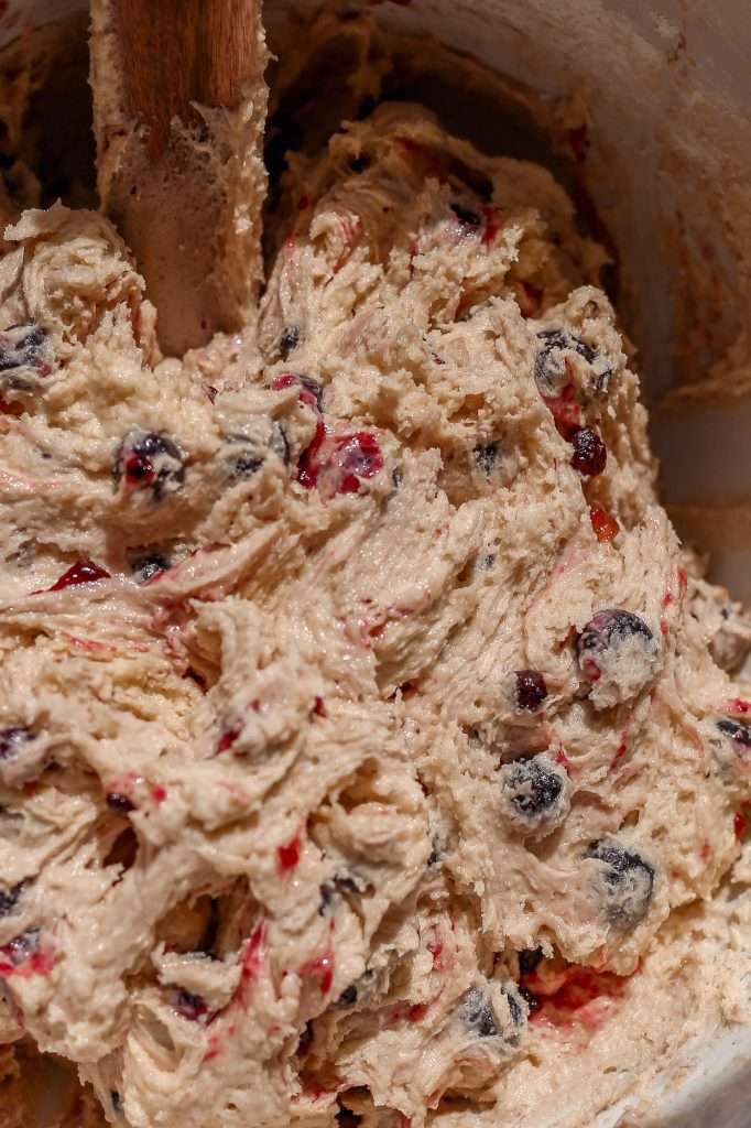 lemon blueberry cookie dough in a white bowl. Blueberries and blueberry preserves are swirled throughout the dough. 