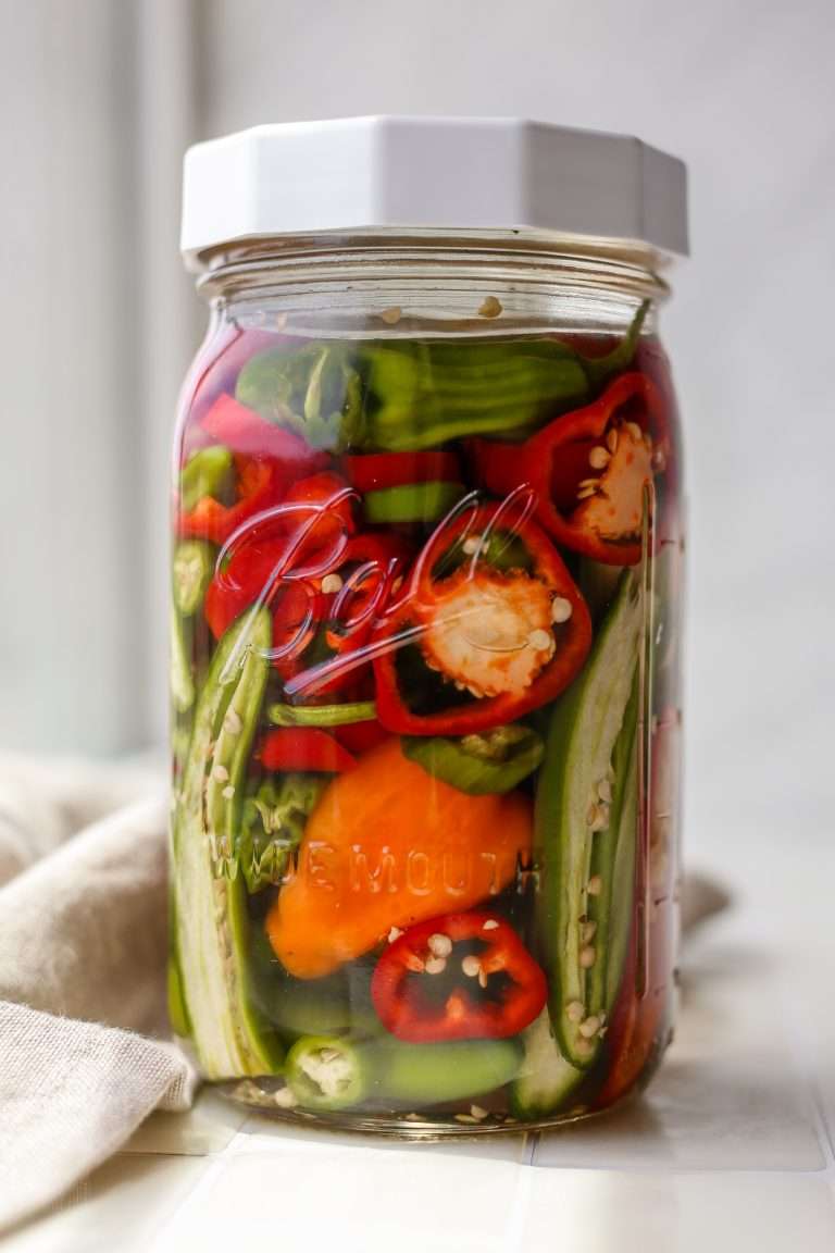 Jar of colorful peppers, including red, orange, and green varieties, in brine for fermentation.