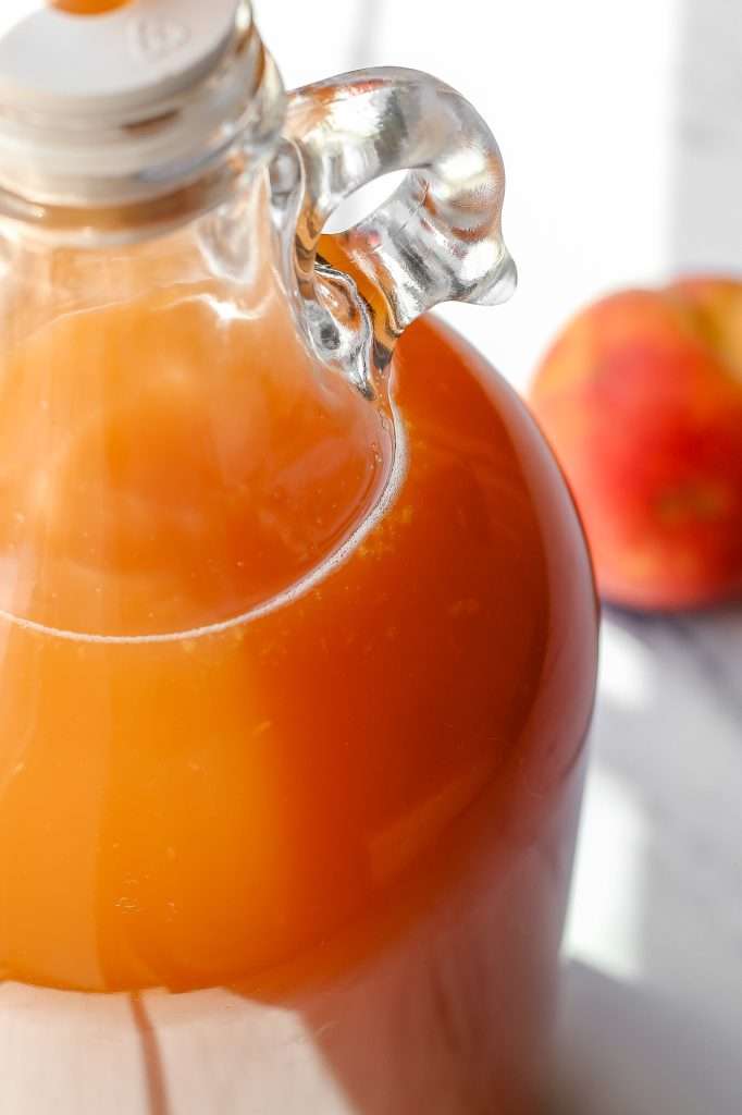 Peach cider fermenting in a 1/2 gallon glass jug with an airlock in the top. the peach hard cider is bubbling. 