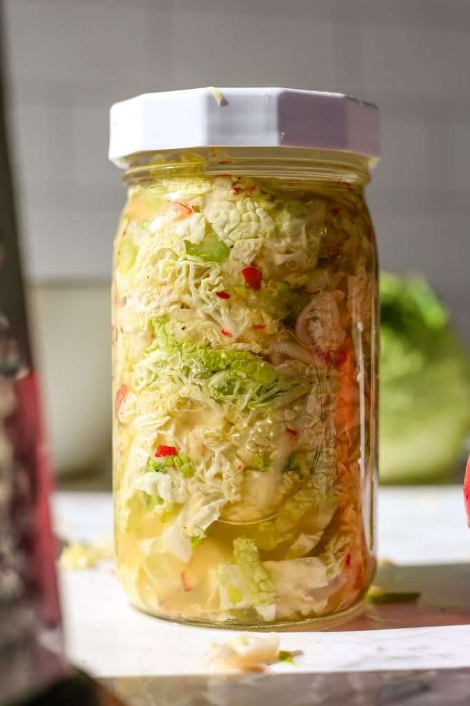 apple sauerkraut in a quart sized glass mason jar with a white plastic lid