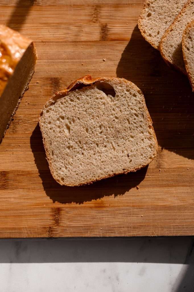 bread machine sourdough sliced on a light brown bamboo cutting board.