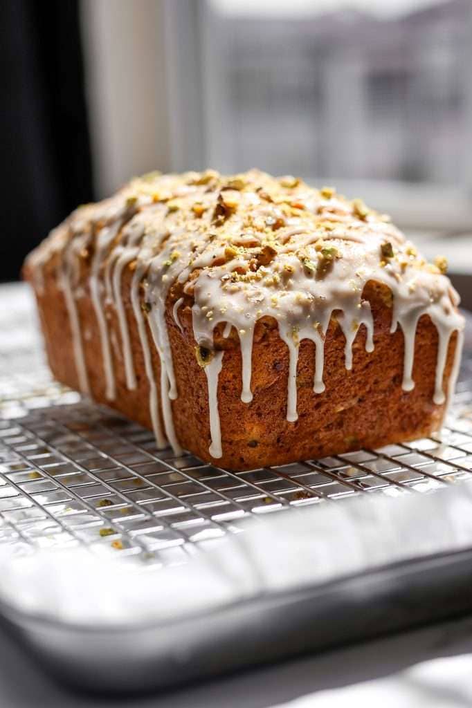 baked zucchini carrot bread on a cooling rack with icing drizzled on top and dripping down the sides.  