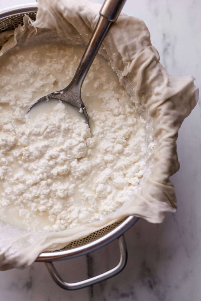 one of the steps in how to make cottage cheese. The curds are straining through a colander lined with butter muslin. 