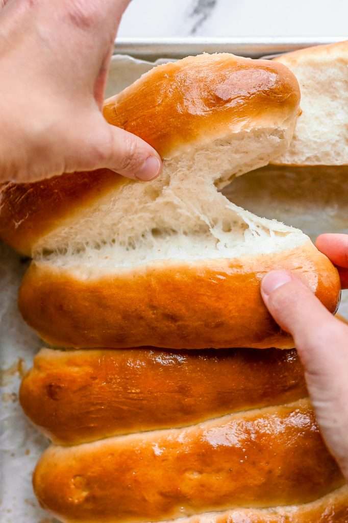 someone pulling apart baked sourdough discard hot dog buns