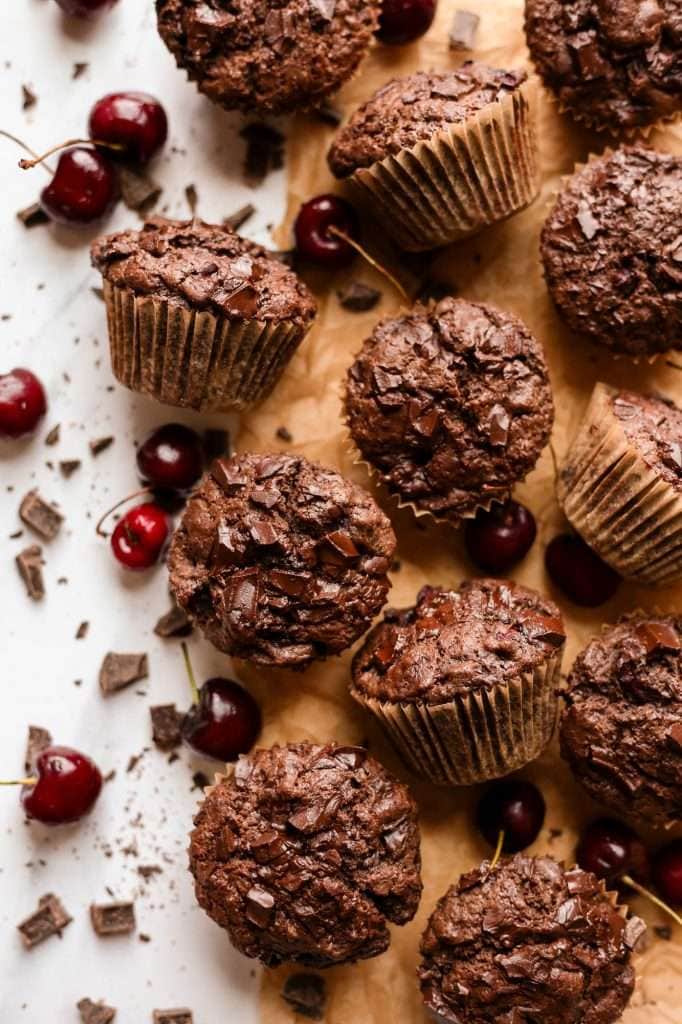 chocolate cherry muffins in brown paper crinkle liners, fully baked and resting on a piece of brown, unbleached, parchment paper. 