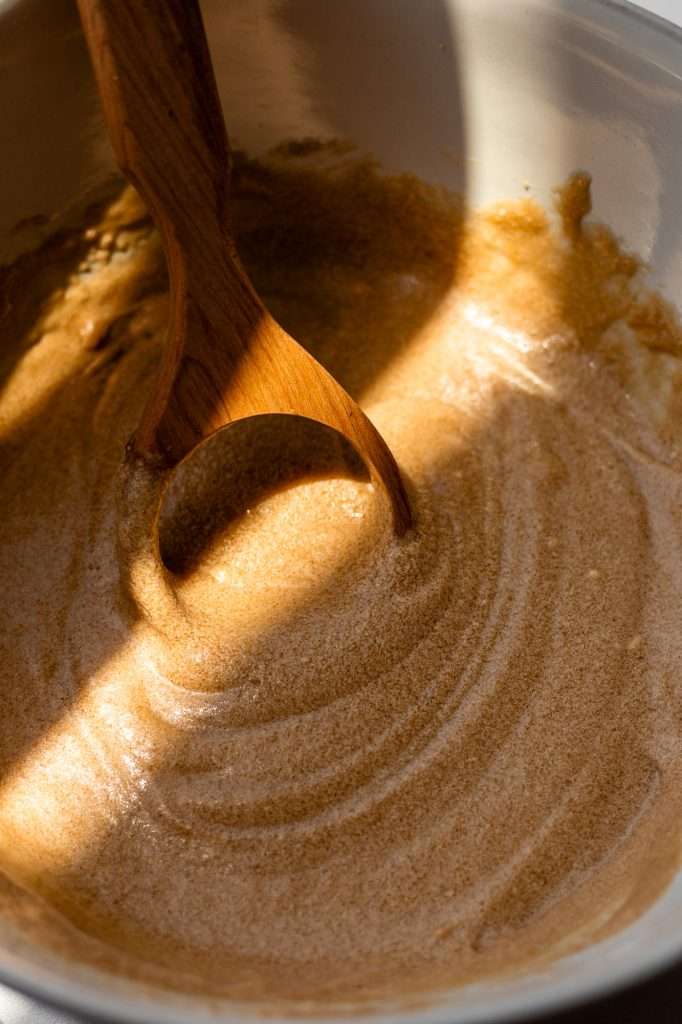 sourdough cinnamon graham crackers wet ingredients creamed together in a white bowl. A wooden danish whisk sits in the bowl. 