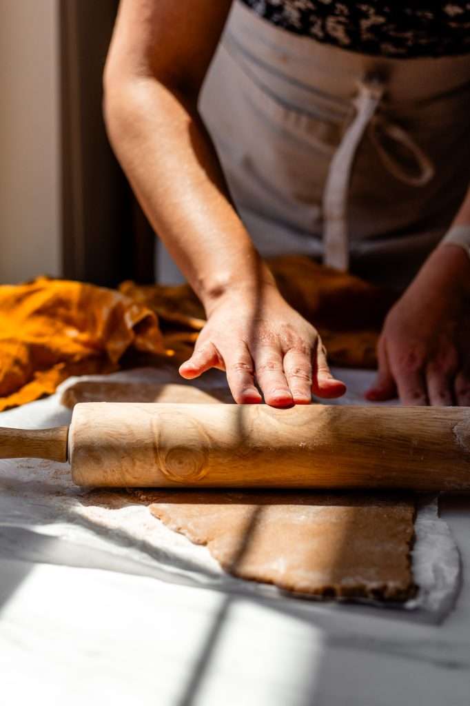 someone using a wooden rolling pin to roll out sourdough graham cracker dough. 