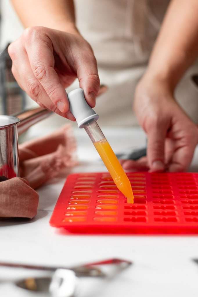 to make protein gummy bears the juice and gelatin mixture is being dispensed into silicone gummy bear molds with a syringe. 