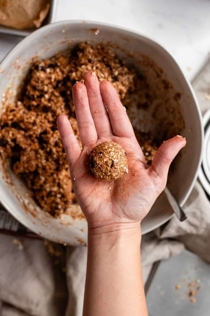 Hand holding a chocolate chip cottage cheese cookie dough bite with the mixing bowl in the background.