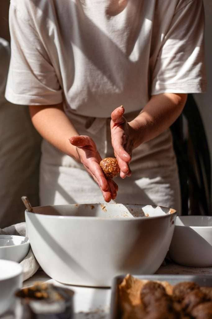 Person shaping cottage cheese cookie dough into bite-sized balls over a mixing bowl.