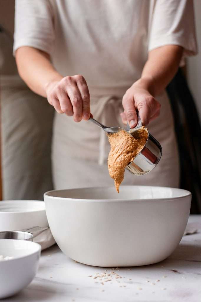 Person spooning peanut butter into a mixing bowl for chocolate chip cottage cheese cookie dough.