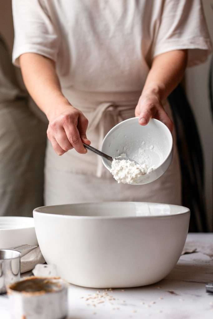 Person adding cottage cheese to a mixing bowl for cookie dough bites.