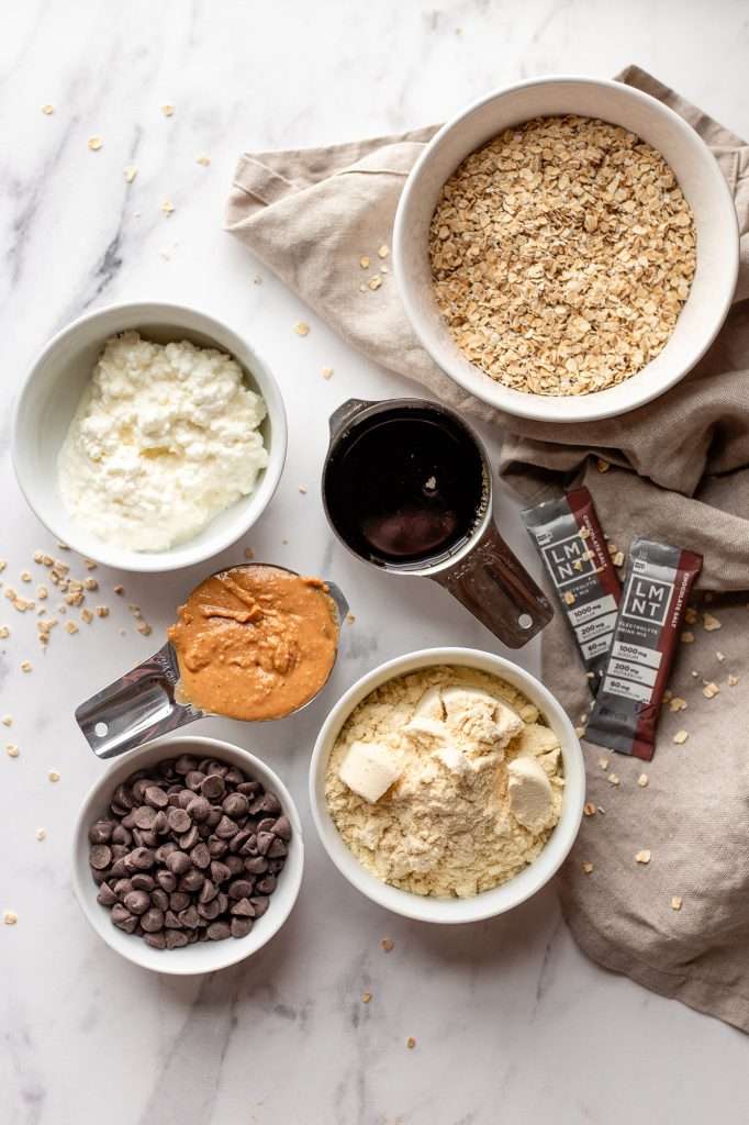 Ingredients for chocolate chip cottage cheese cookie dough, including oats, cottage cheese, peanut butter, protein powder, maple syrup, chocolate chips, and LMNT electrolytes.