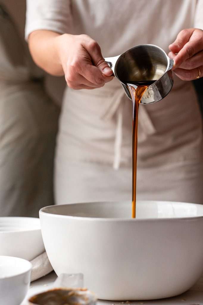 Person pouring maple syrup into a mixing bowl for cookie dough bites.