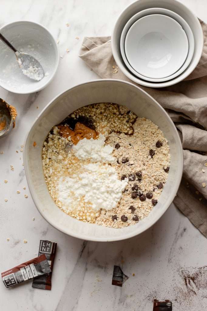 Mixing bowl filled with cottage cheese, peanut butter, oats, chocolate chips, protein powder, and maple syrup.