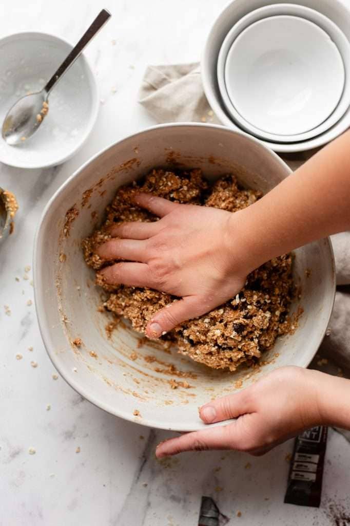 Person mixing chocolate chip cottage cheese cookie dough ingredients by hand in a bowl.