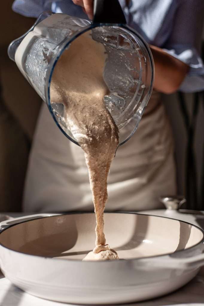 Pouring blended gouda and cottage cheese sauce from a blender into a cooking pot.