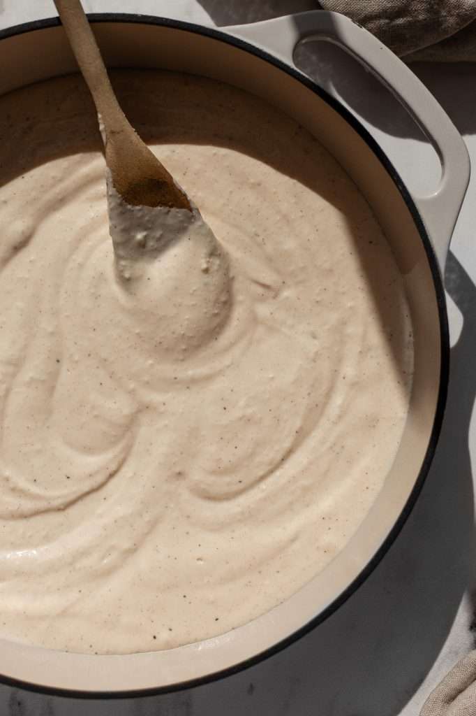 Close-up of a spoon stirring a thick, creamy cheese sauce in a pot.