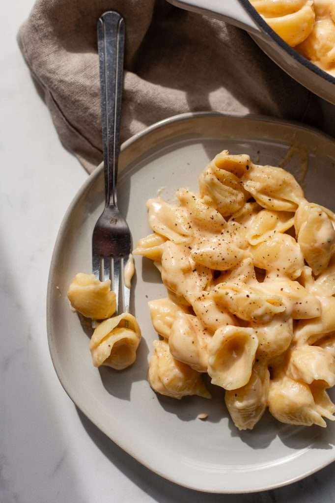 Plate of creamy cottage cheese mac and cheese topped with cracked black pepper, with a fork holding a piece of shell pasta.