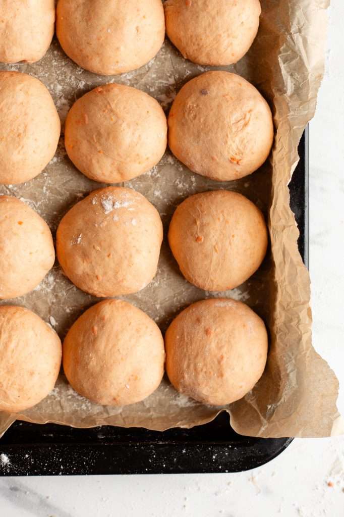 sweet potato dinner rolls shaped and ready for a final rise before baking. The rolls are placed in a 9x9 pan lined with parchment paper. 