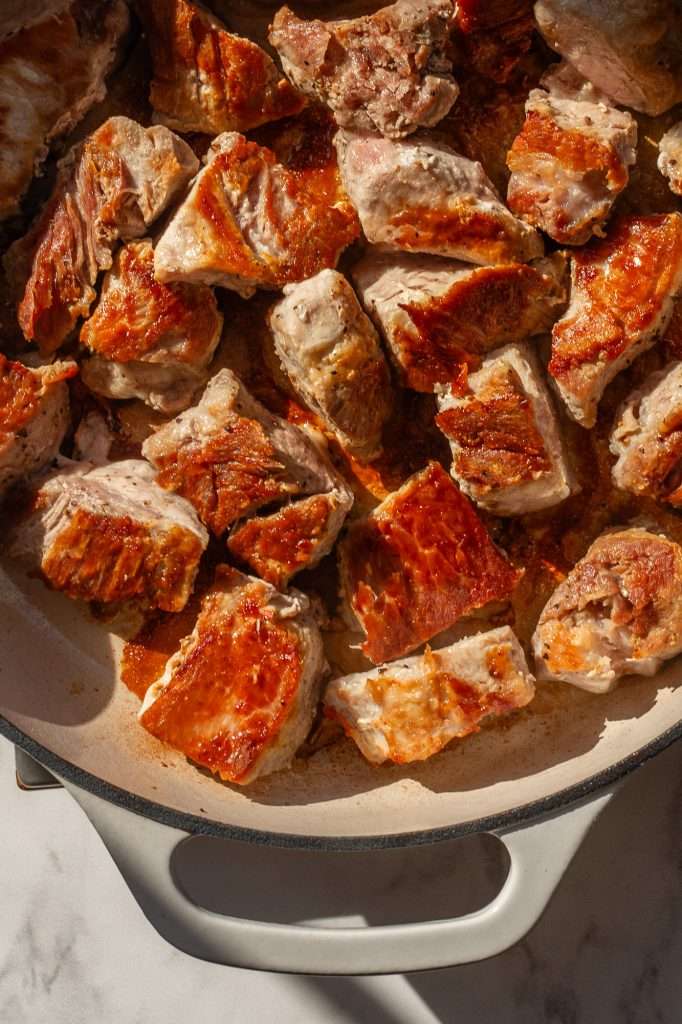 Seared pork loin cubes in a white Dutch oven, showing golden seared edges after cooking.