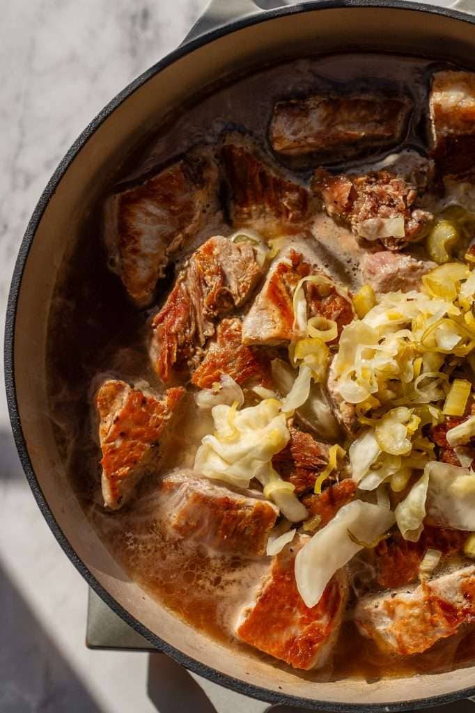 Partially cooked pork loin chunks in a Dutch oven, topped with sauerkraut, ready for braising