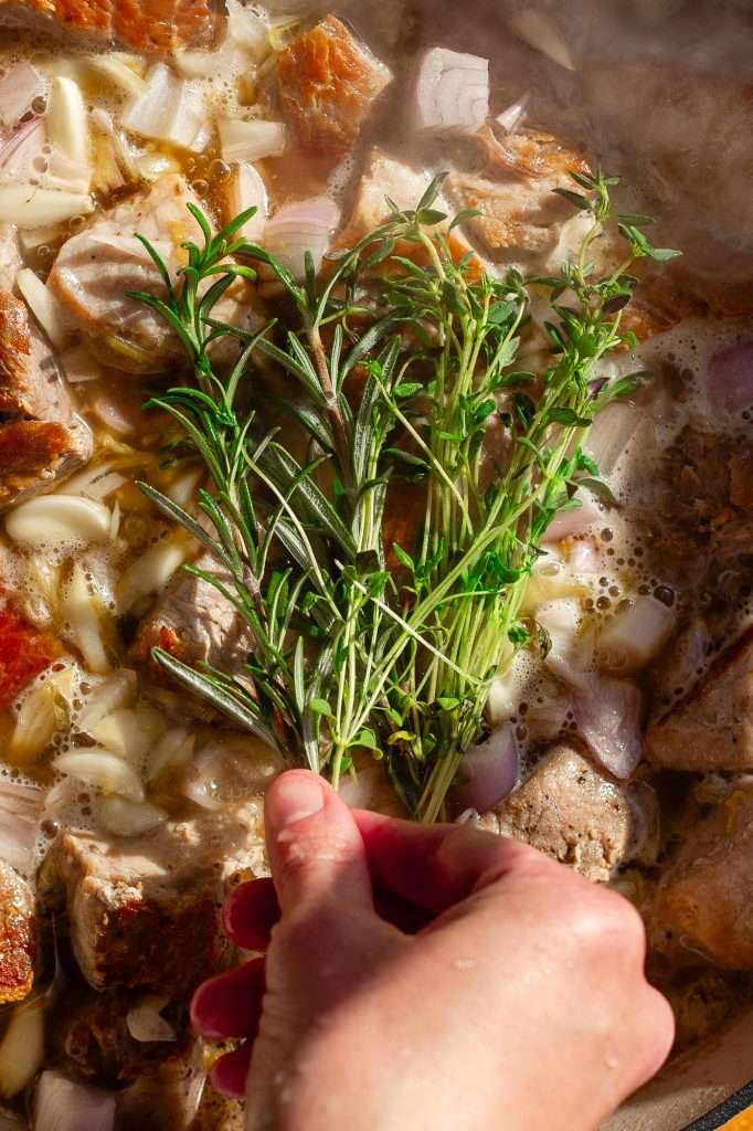 decorative image of thyme and rosemary brushing the seared pork.