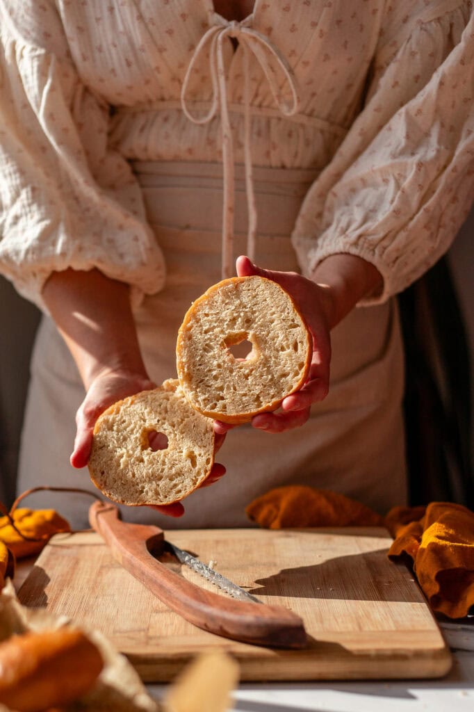 Two halves of a sliced sourdough bagel held in hand, showing its soft and airy interior.